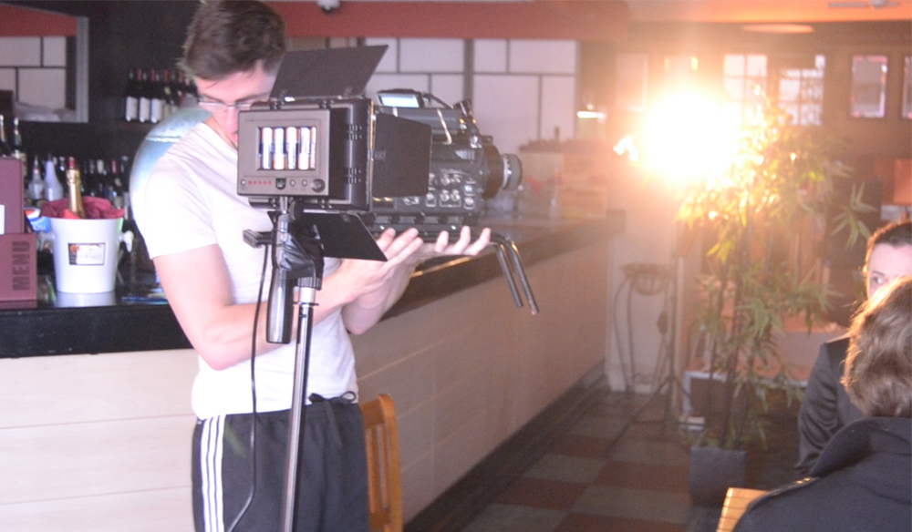 A man in a white shirt operating a video camera in a restaurant setting. 